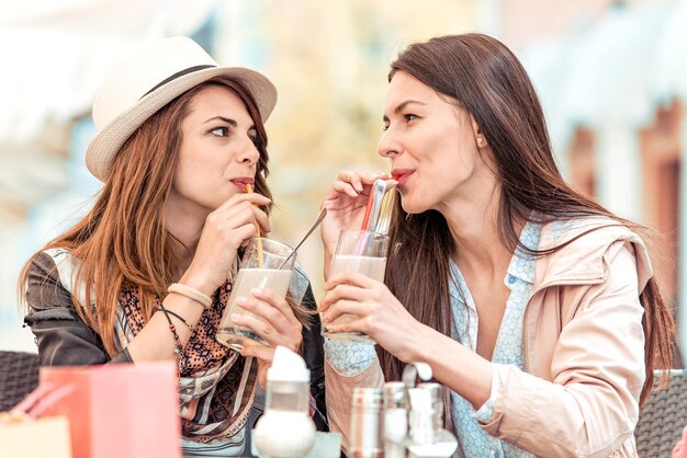 Twee mooie vrouwen die limonade drinken en kletsen in café