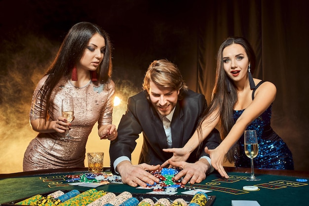 Twee mooie vrouwen en jonge man spelen op pokertafel in casino, focus op man en brunette