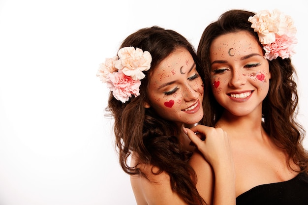 Twee mooie vrouwen met donkerbruin haar, roze bloemen in hun haar en schilderijen op het gezicht zien eruit als een tweeling