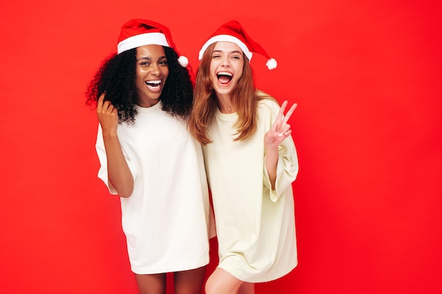 Twee mooie vrouwen vieren new year.happy prachtige vrouw. ze hebben plezier op oudejaarsavond feest. vakantie feest. charmante modellen in santa claus hoeden lachen in de buurt van rode muur