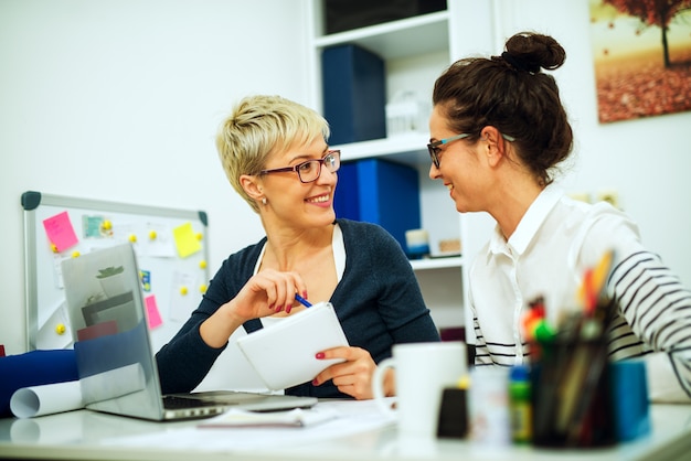 Twee mooie vrouwencollega van middelbare leeftijd die samen werken en elkaar kijken terwijl zij aan het bureau in het bureau zitten.