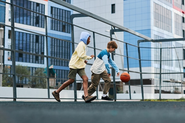 Twee multiculturele jongens in activewear die buiten basketballen