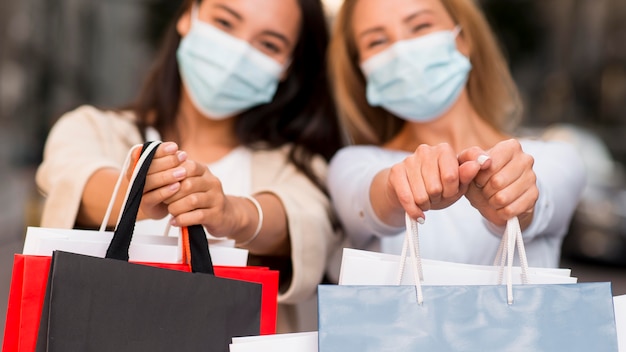 Twee onscherpe vrouwen met medische maskers poseren samen met boodschappentassen