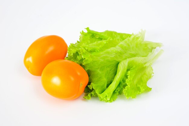 twee oranje tomaten met groene salade bladeren geïsoleerd op een witte achtergrond