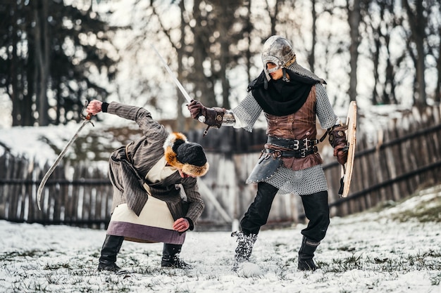 Twee oude krijgers in harnas met wapens vechten met zwaarden in de sneeuw