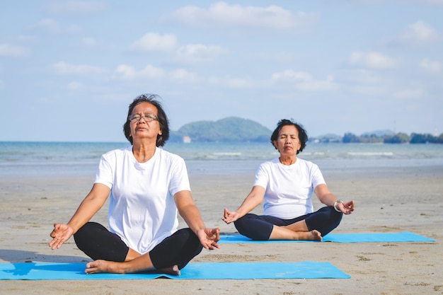 Twee oudere vrouwen oefenen op het strand aan zee Zitten en yoga doen