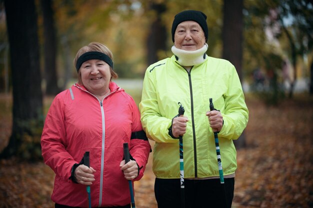 Twee oudere vrouwen staan in een park met stokken voor nordic walking mid shot