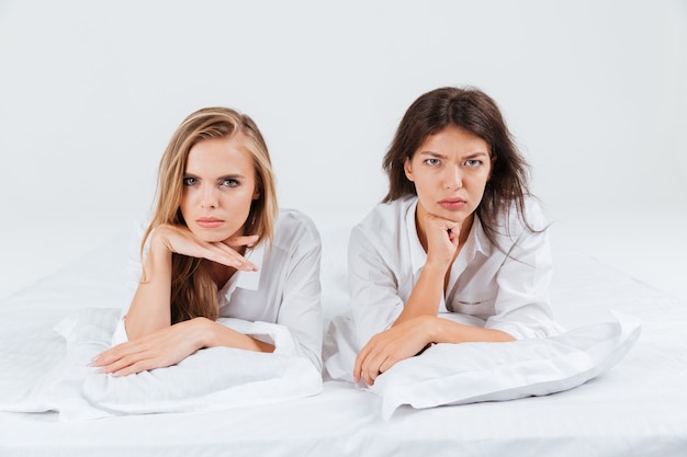 Twee overstuur ongelukkige vrouwen die samen in bed liggen en naar de camera kijken