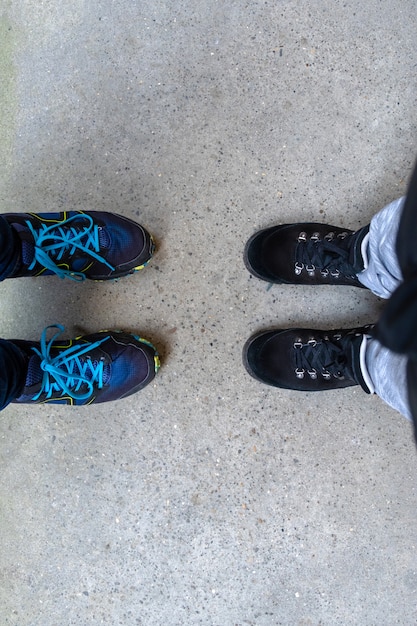 Twee paar benen in laarzen om te wandelen staan op de grijze stoep.