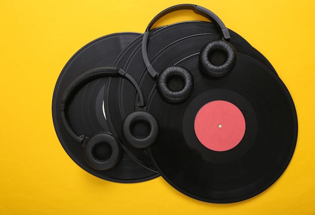 Twee paar zwarte stereohoofdtelefoons en vinylplaten op gele achtergrond