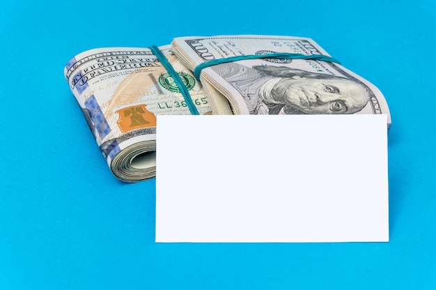 Foto twee pakken gevouwen dollarbiljetten met blanco visitekaartje op een blauwe achtergrond
