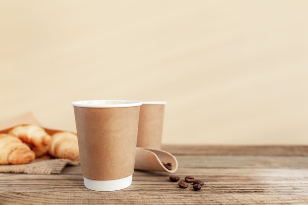 Twee papieren kopjes koffie croissants koffiebonen en lepel aan houten tafel