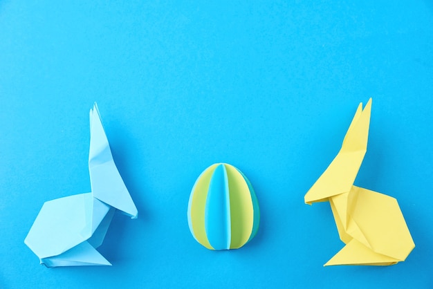 Twee papieren origami Pasen konijnen en gekleurd ei op blauw