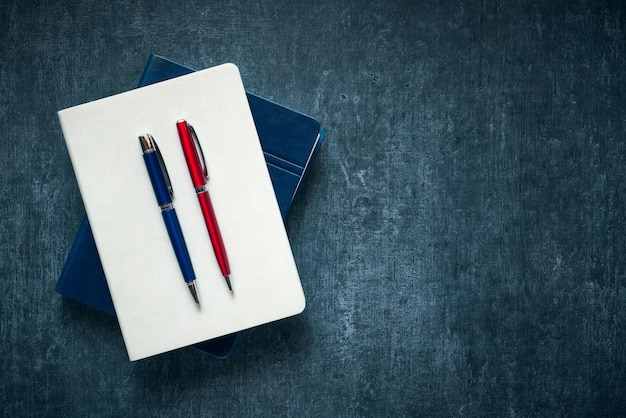 Twee pennen blauw en rood rustend op een witte gesloten notebook donkere grunge achtergrond mockup