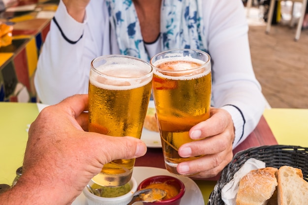 Twee personen genieten van een glaasje koud bier met wat hapjes. verfrissend en goudkleurig bier. bar tafel