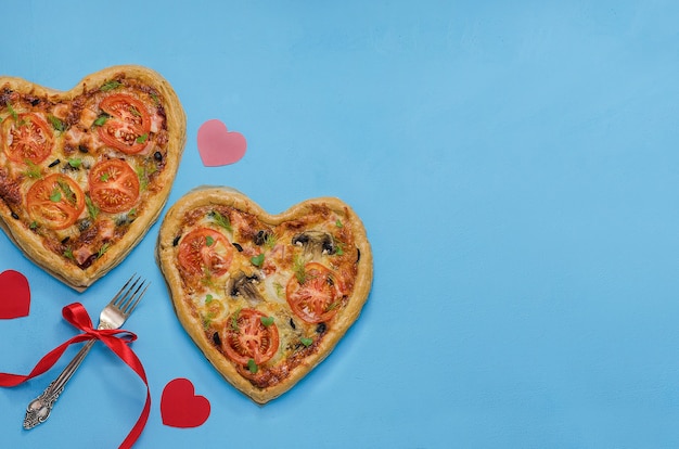 Twee pizza in de vorm van een hart op een blauwe tafel met rode harten met kopie ruimte. Bestel pizza voor een romantisch diner op Valentijnsdag. Liefde.