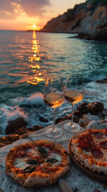 Twee pizza's en glazen wijn op het strand bij zonsondergang.