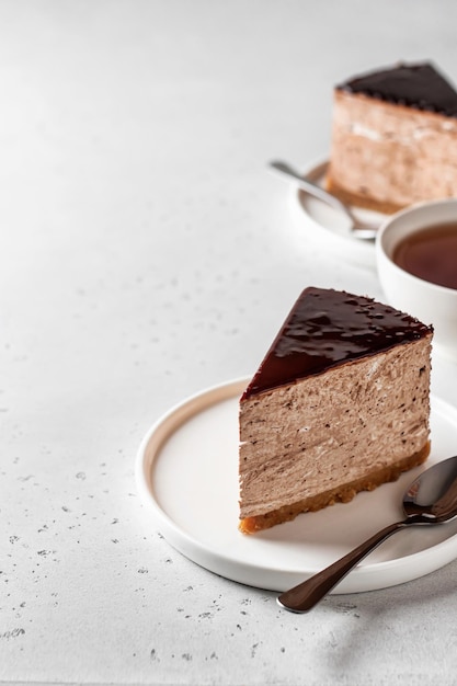 Twee plakjes chocolade cheesecake op witte borden met een kopje thee op een witte achtergrond