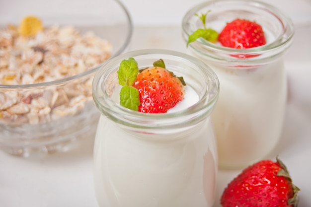 Twee porties natuurlijke zelfgemaakte yoghurt in een glazen pot met verse aardbeien en muesli in de buurt