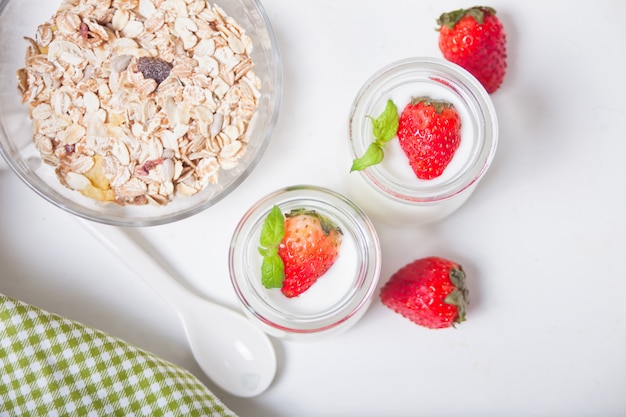 Twee porties natuurlijke zelfgemaakte yoghurt in een glazen pot met verse aardbeien en muesli in de buurt