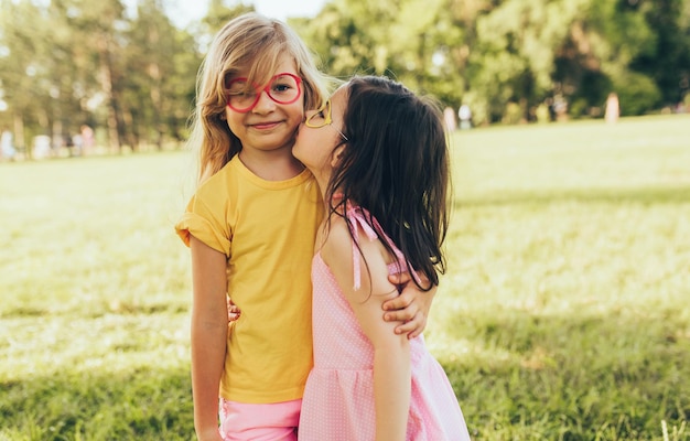Twee positieve kinderen delen liefde en vriendschap Twee kleine meisjes genieten van de zomer in het park Twee zussen hebben plezier in zonlicht buitenshuis Jeugd en vriendschap concept
