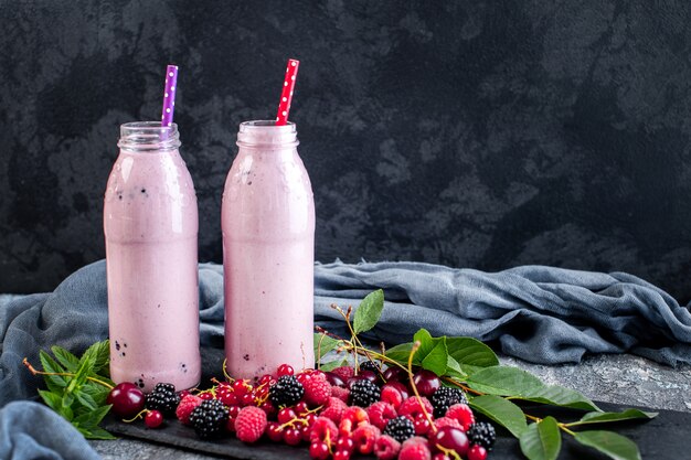 Twee potten milkshake of smoothie met veenbessen, aardbeien en bosbessen staan op stenen oppervlak