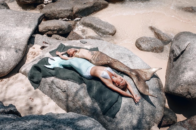 Twee prachtige zeemeerminnen zonnebaden op stenen op een visnet, mythische wezens