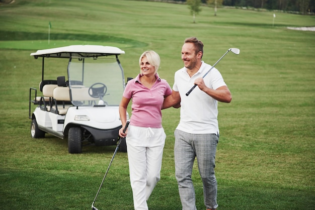 Twee professionele golfers, een vrouw en een man gaan samen naar de volgende hole. Liefhebbers knuffelen en glimlachen, ze hebben een date