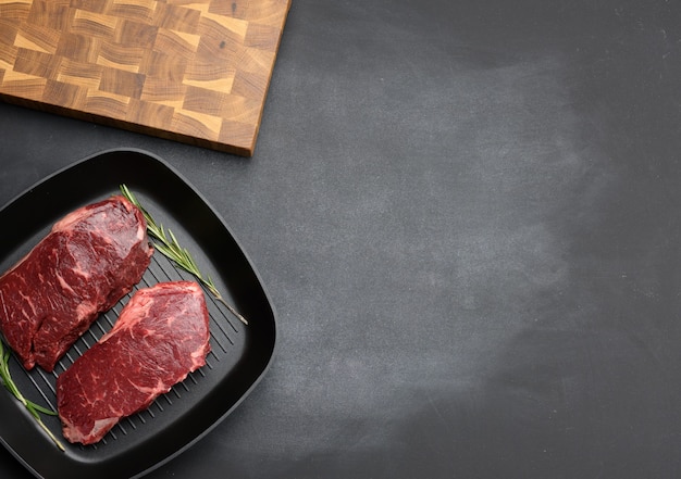 Twee rauwe stukjes rundvlees in een zwarte vierkante grillpan, steaks op een zwart oppervlak, bovenaanzicht, kopieerruimte