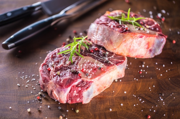 Twee rauwe stukken rundvlees schacht op houten slager bord met vork en mes.