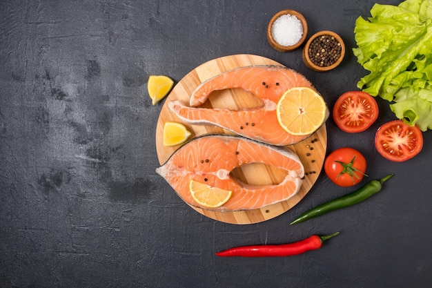 Twee rauwe zalmsteaks op een rond keukenbord met ingrediënten voor het koken bron van omega 3 en verzadigde vetten bovenaanzicht zwarte achtergrond