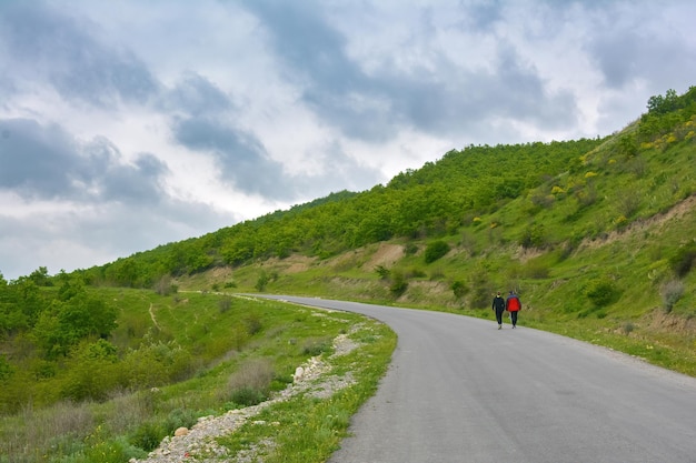 Twee reizigers lopen langs een asfaltweg in de groene bergen