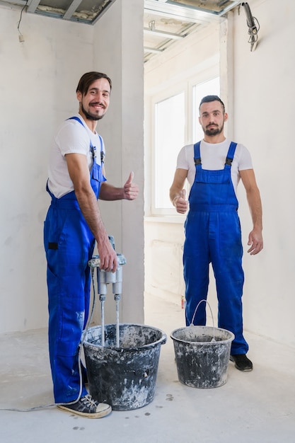 Twee reparateurs in blauwe overall bereiden cement in een emmer voor