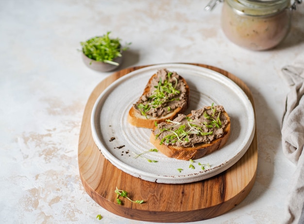 Twee rillettes van de toostskip (pastei) op wit brood met spruiten op witte plaat op een houten scherpe raad. copyspace