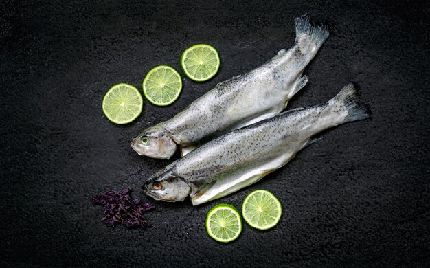 Twee rivierforellen en ingrediënten op een zwarte steenlijst, hoogste mening.