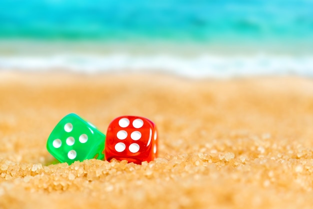 Twee rode en groene dobbelstenen in het zand op de achtergrond van strand en zee