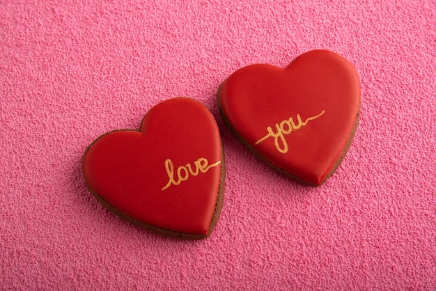 Twee rode koekjes in de vorm van harten met de inscriptie love you op roze achtergrond