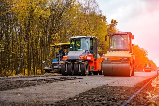 Twee rode speciale auto's die nieuw asfalt aan het bestraten zijn, rijden in de ene in de buurt van de andere nieuwe wegenbouw selectieve focus