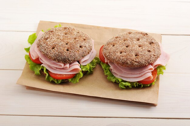 Twee ronde sandwich van roggebrood met ham, tomaat en sla op papier