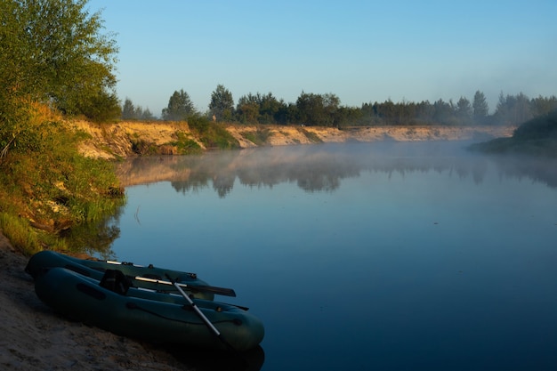 Twee rubberboten met visgerei in de vroege ochtend tijdens de mist, geparkeerd aan de oevers van de rivier.