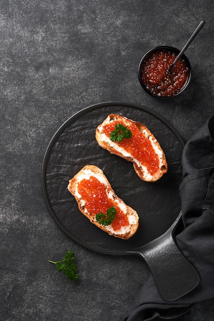 Twee sandwiches met rode kaviaar Zalm rode kaviaar in kom en sandwiches server op oude ijzeren plaat op oude zwarte tafel achtergrond Bovenaanzicht kopie ruimte