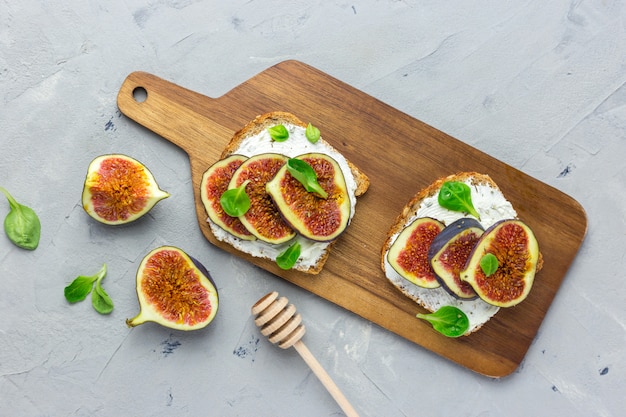 Twee Sandwiches met roomkaas, vijgen, honing en bladsalade dienden op de houten rustieke scherpe raad op grijs