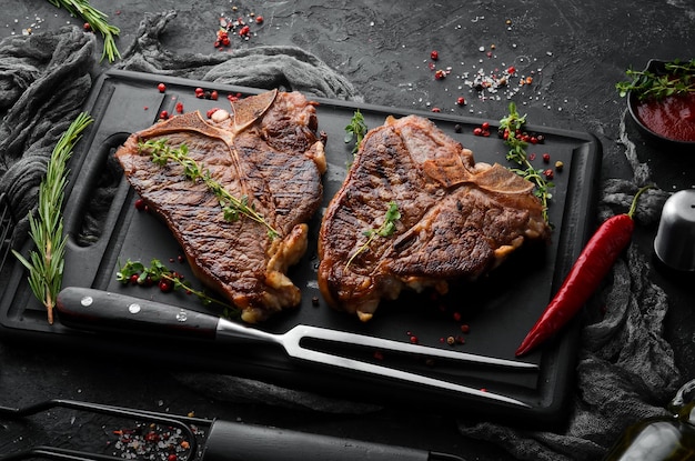 Twee sappige gegrilde steaks met specerijen en kruiden op een zwarte achtergrond Bovenaanzicht Rustieke stijl