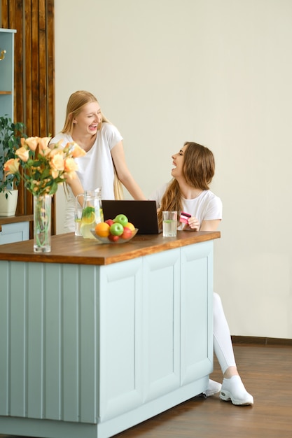 Twee schattige jonge vrouwen die online winkelen, goederen zoeken en bespreken