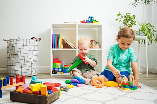 Twee schattige jongens die naast elkaar zitten, elk met hun eigen speelgoed Kinderen van verschillende leeftijd kunnen vreedzaam samen spelen Relatie tussen broers en zussen