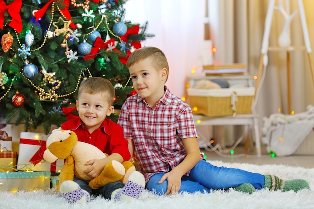 Twee schattige kleine broers met teddybeer op kerstboomachtergrond Christmas