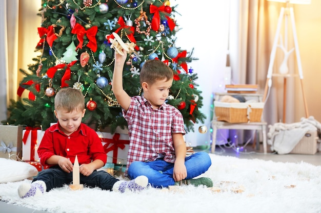 Twee schattige kleine broers spelen met houten vliegtuig op kerstboom achtergrond