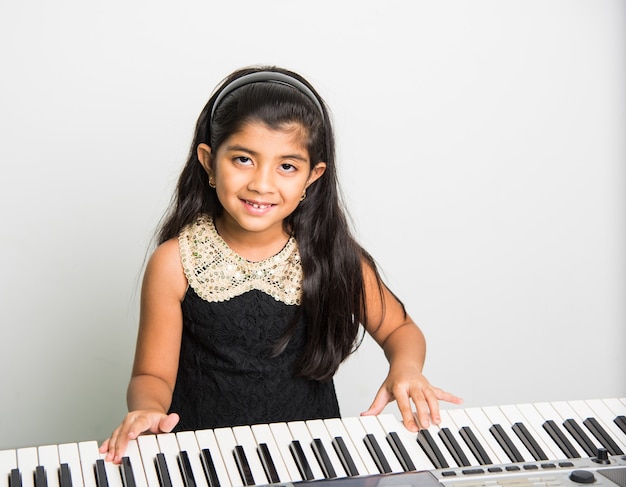 Twee schattige kleine Indiase of Aziatische meisjes spelen piano of keyboard, een muziekinstrument, op witte achtergrond