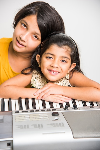 Twee schattige kleine indiase of aziatische meisjes spelen piano of keyboard, een muziekinstrument, op witte achtergrond