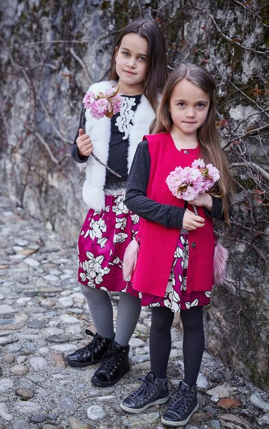 Twee schattige kleine meisjes houden boeketten bloemen op de grijze rotsachtergrond.